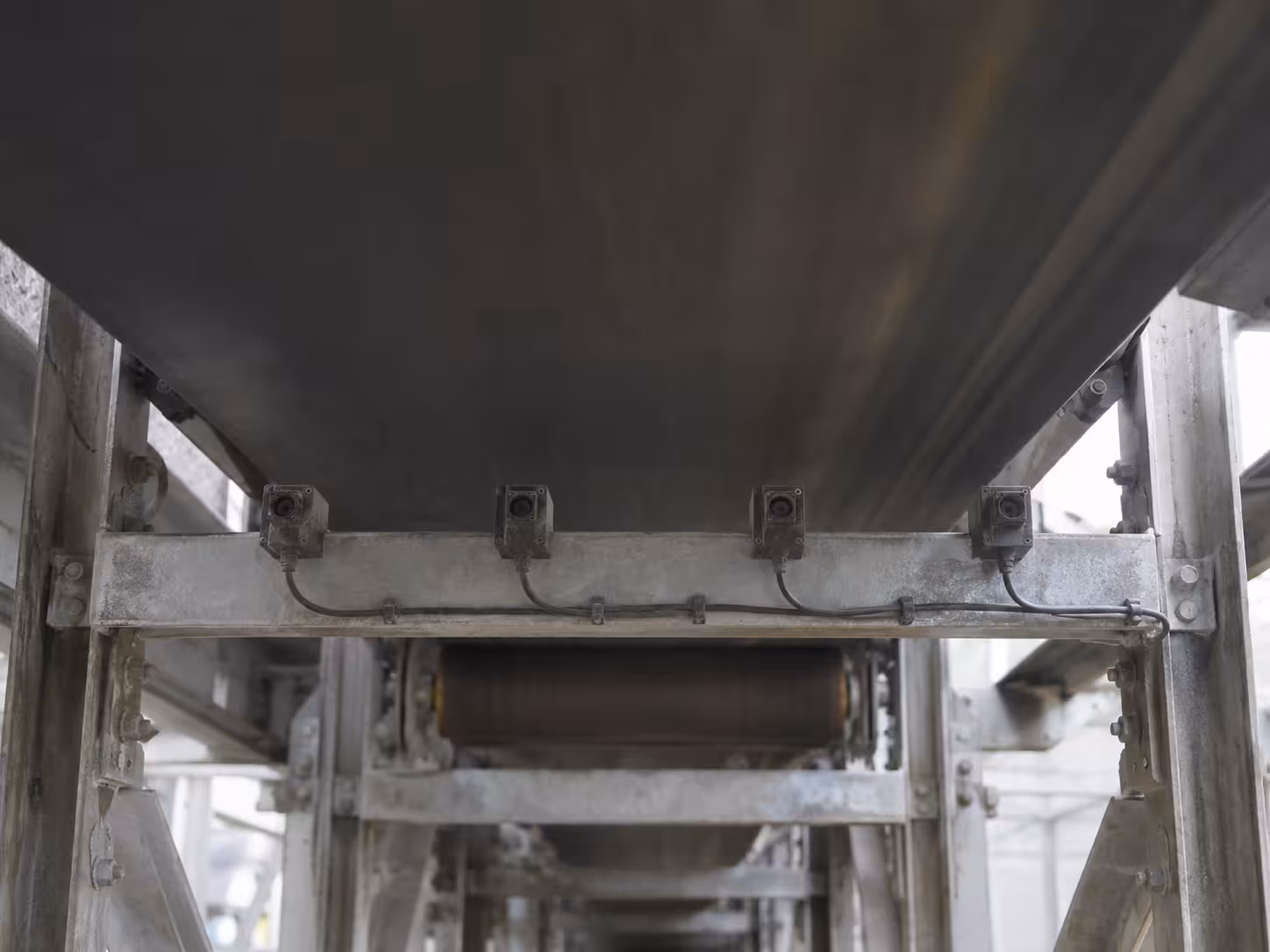 A row of sensors under the conveyor scans the belt from below and raises the alarm the moment it finds damage. (AI-generated image)